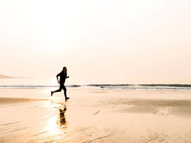 silhouette of a person running on the beach within the reflection of the rising sun