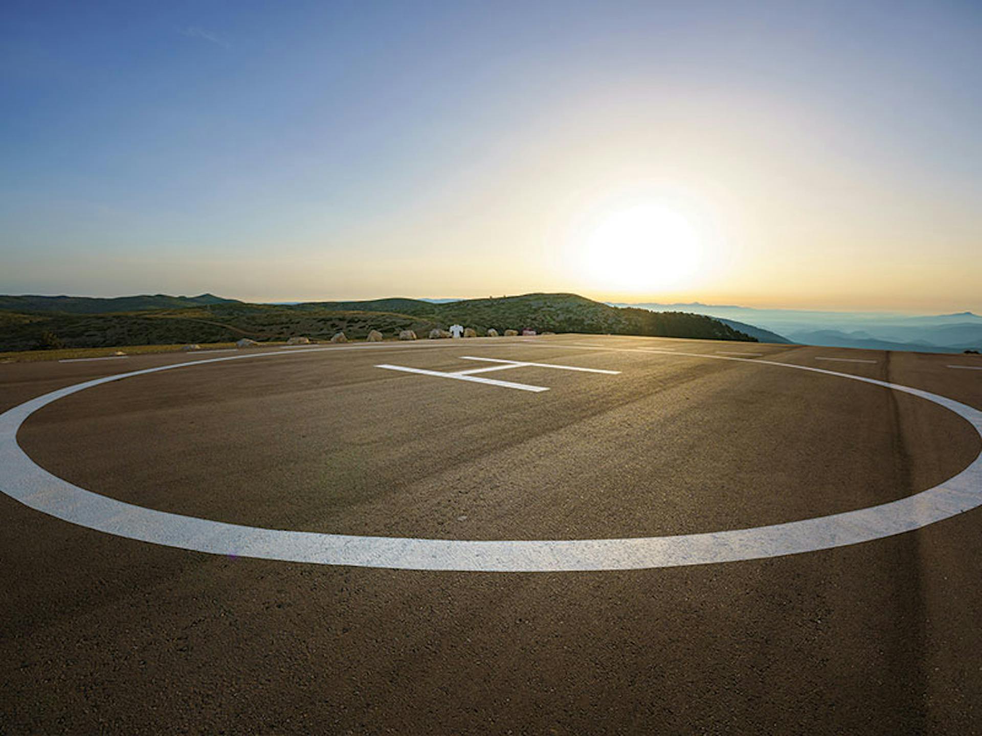 A helicopter pad with a view of rolling hills and a sun rise