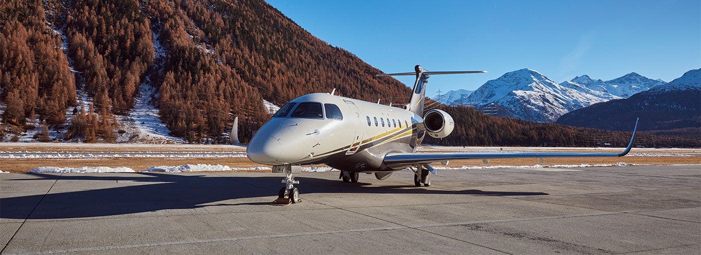A flexjet aircraft sits on a tarmac near mountains sprinkled with snow and covered with trees