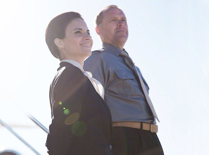 two crew members stare off camera, one smiling and one stern