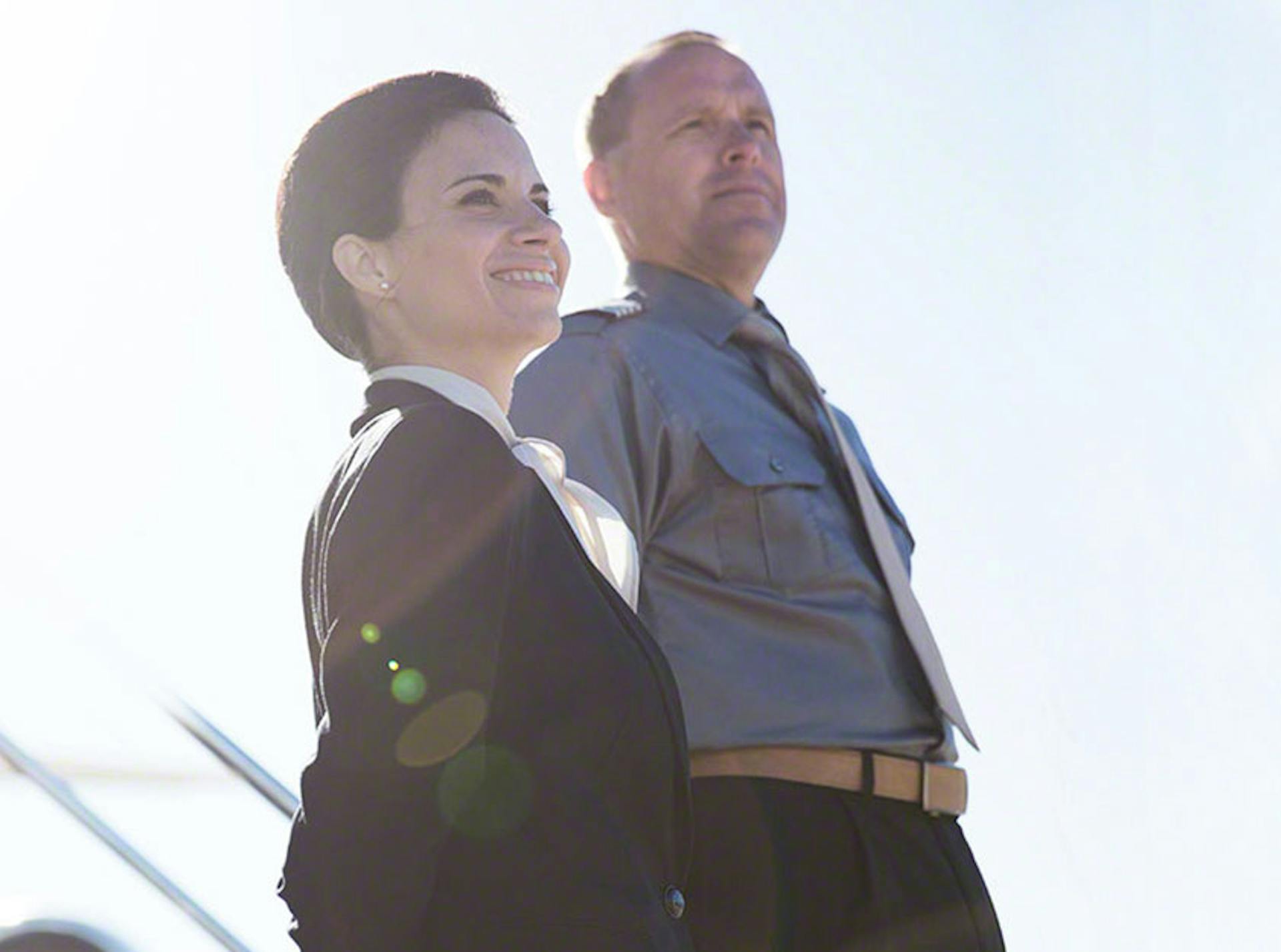 two crew members stare off camera, one smiling and one stern