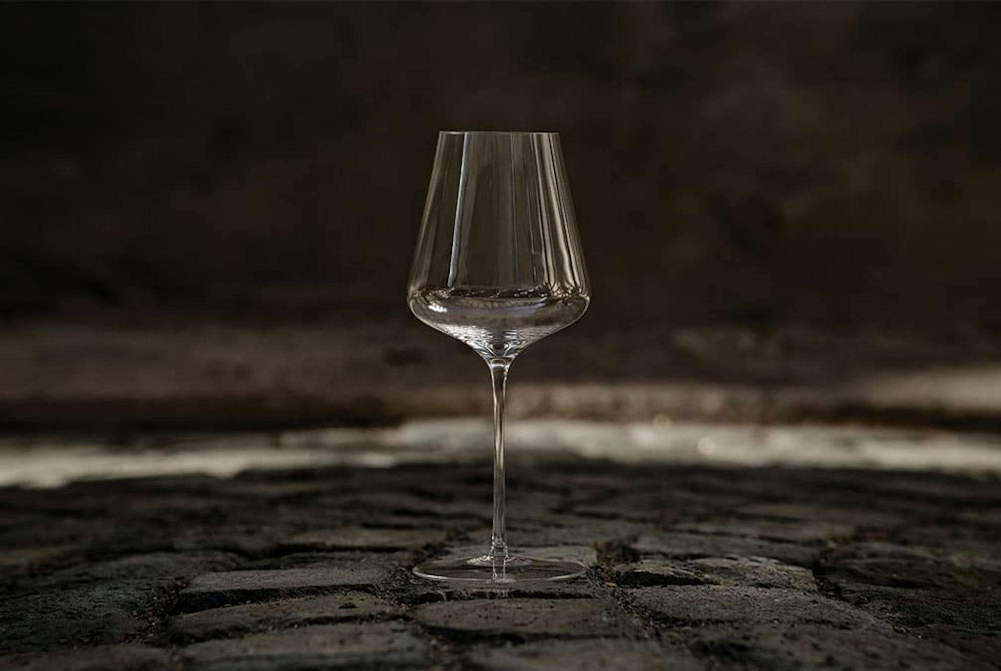 A wine glass sits outside in the dark on a stone path