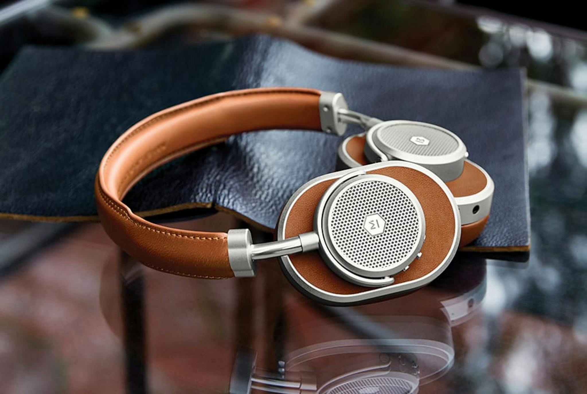 a pair of headphones, leather and light brown sitting on top of a folder black book on a glass table