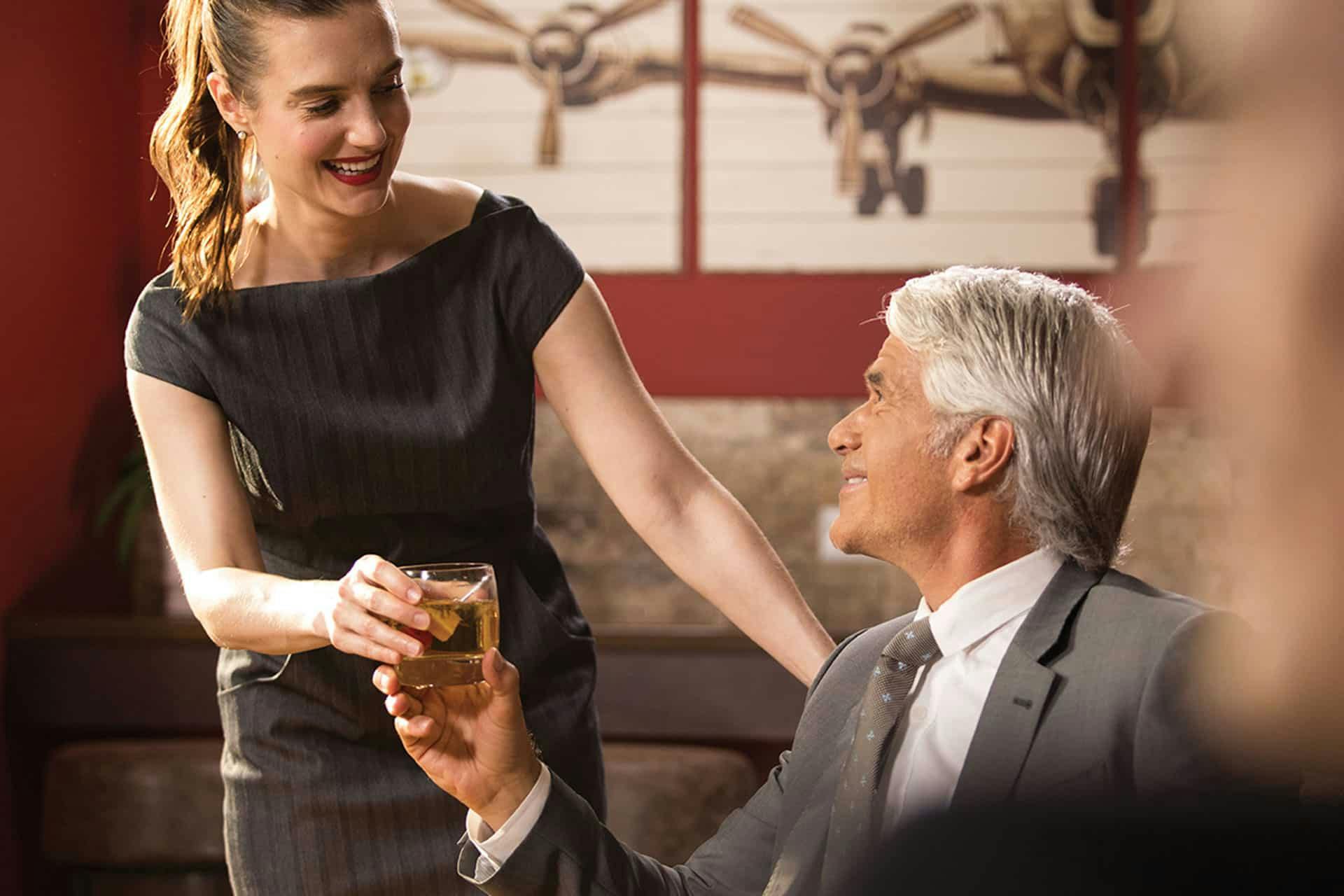 Inside the private terminal at White Plains a woman hands a seated man a drink as they smile at each other