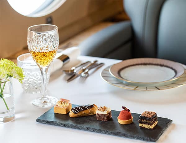 A glass, silverware and plate sit a top a table on a private jet with the focus being a plate of decadent desserts