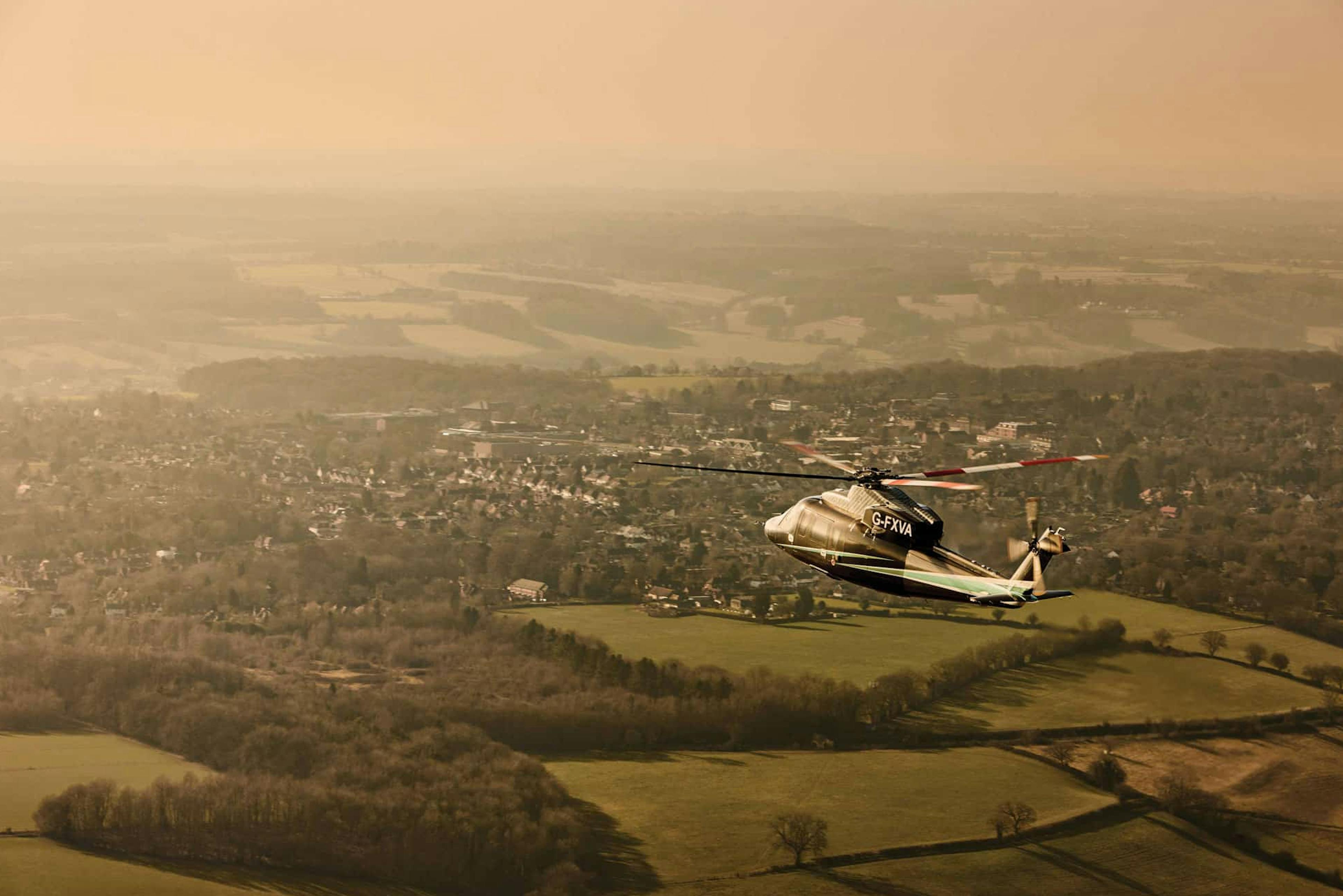 A flexjet helicopter flies over a suburban landscape with hazy skies 