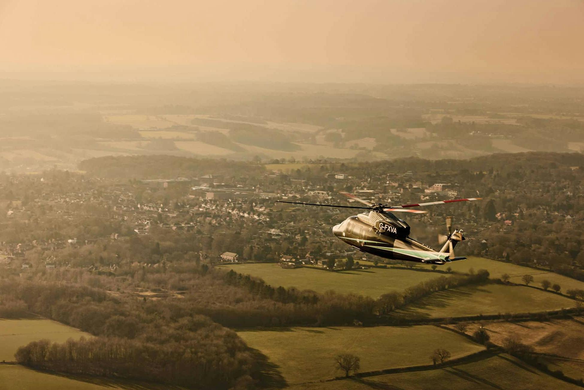 A flexjet helicopter flies over a suburban landscape with hazy skies