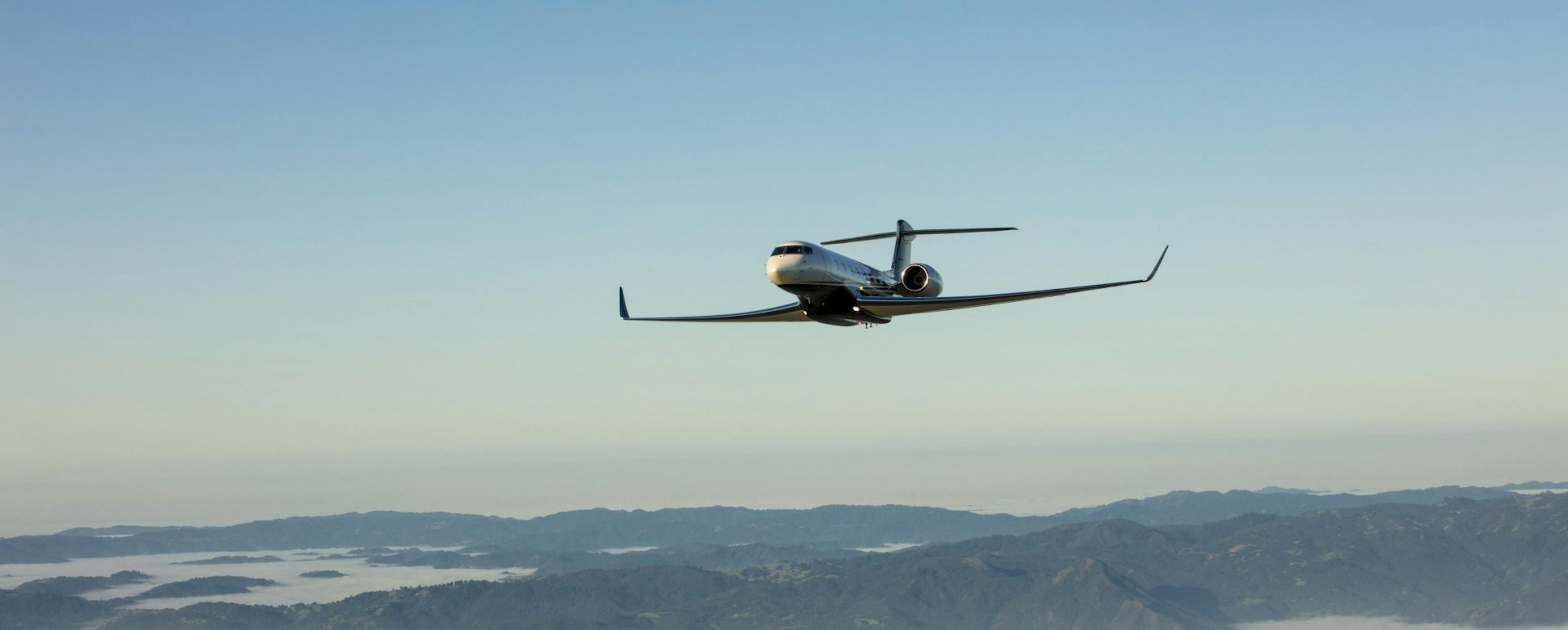 Aircraft flies over mountains and bays among blue skies on the horizon.