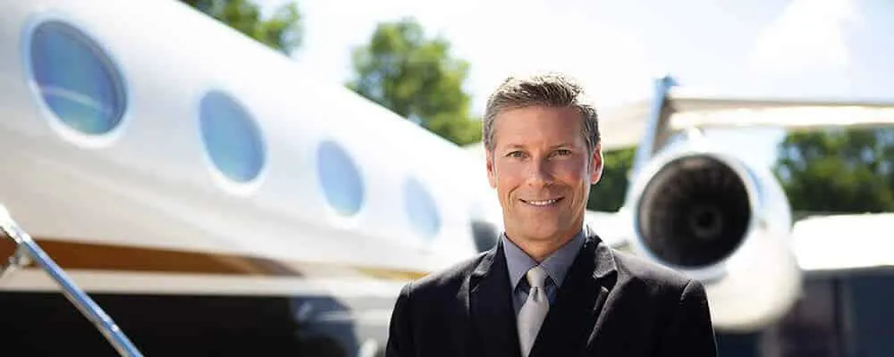 a pilot standing in front of a private jet and smiling