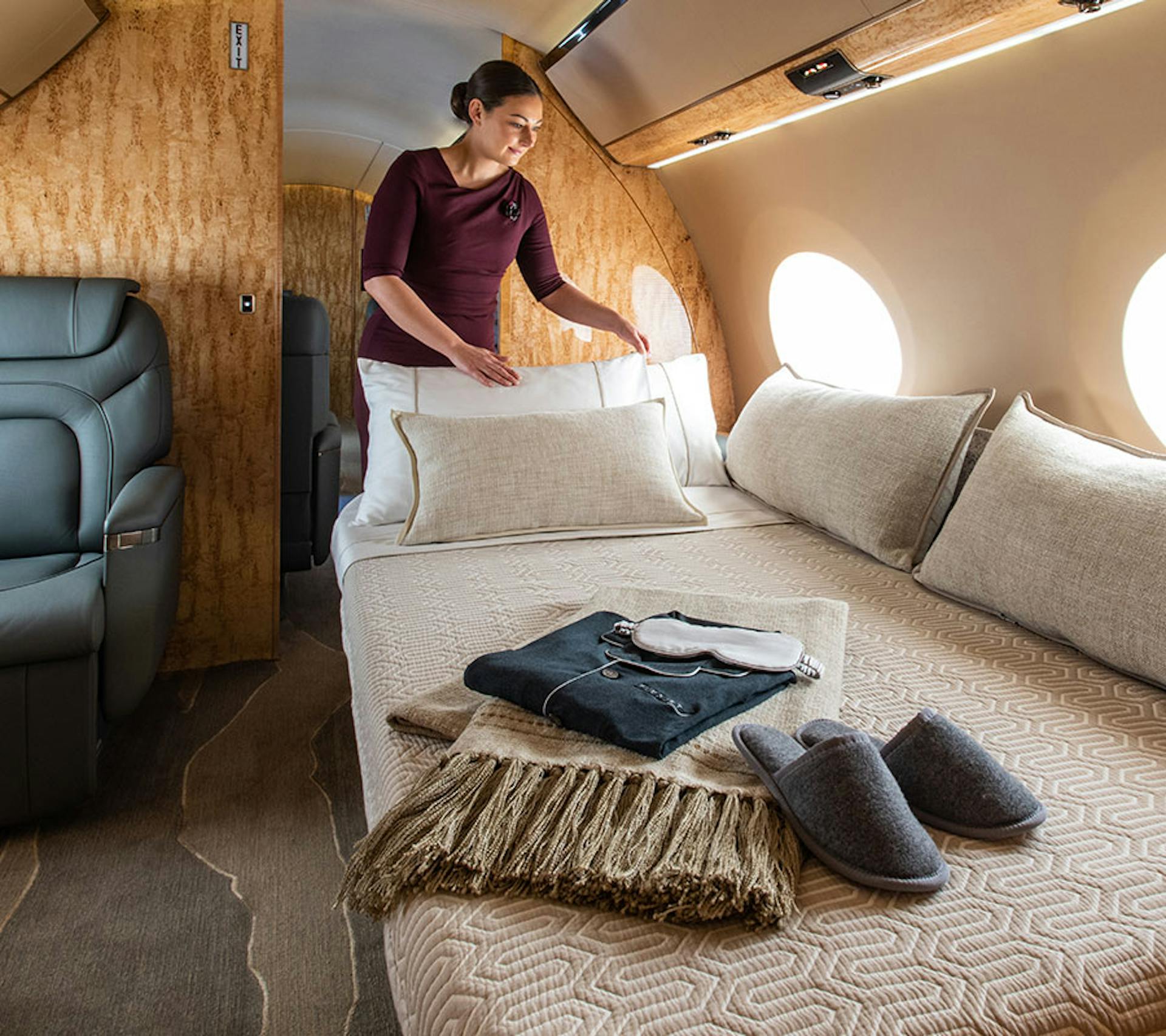 someone setting the pillows on a private jet with slippers, eye mask and other items on the day bed