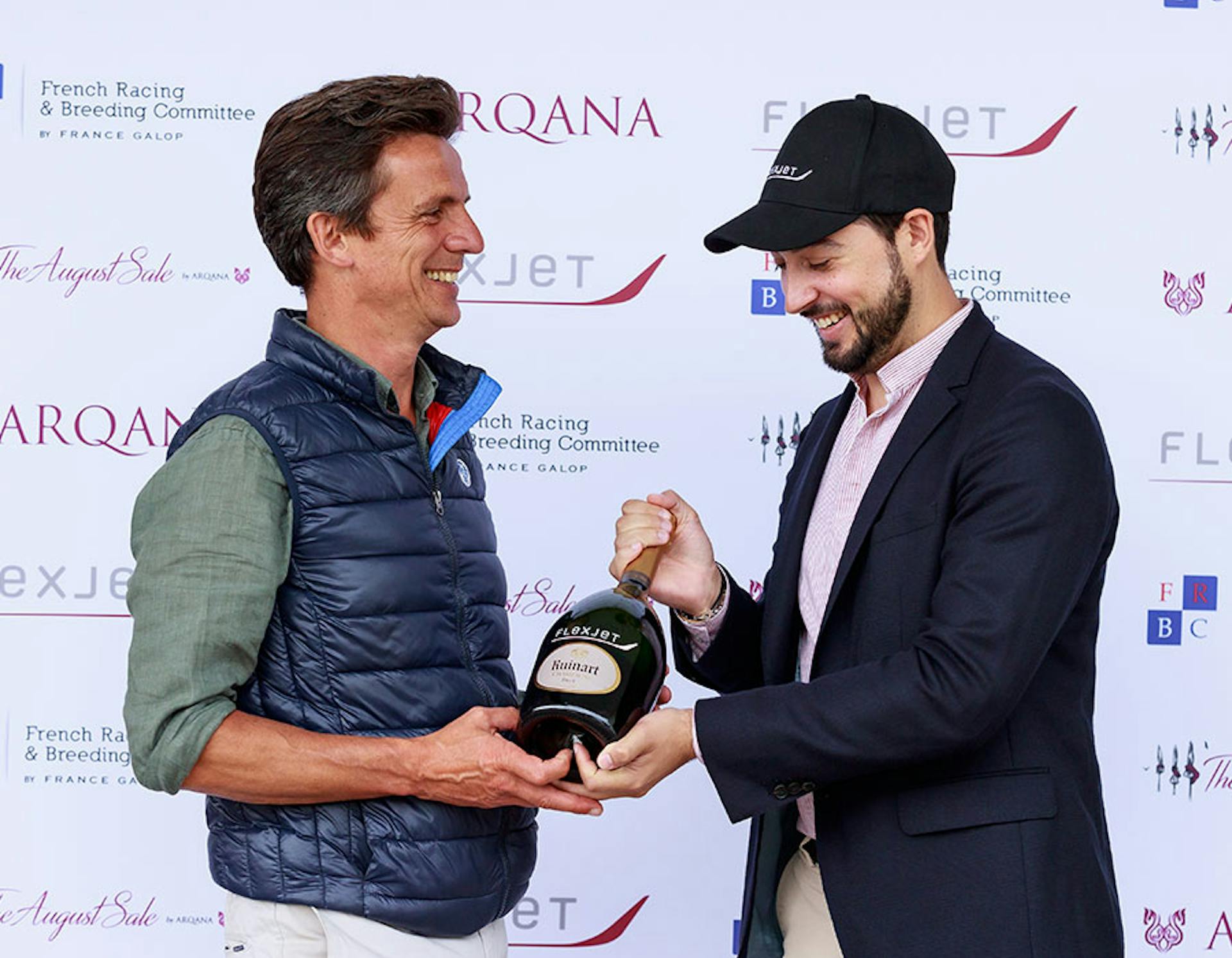 Two men pose with a large bottle of champagne