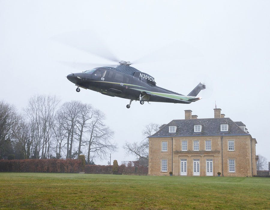 s76 landing on the lawn of a large house