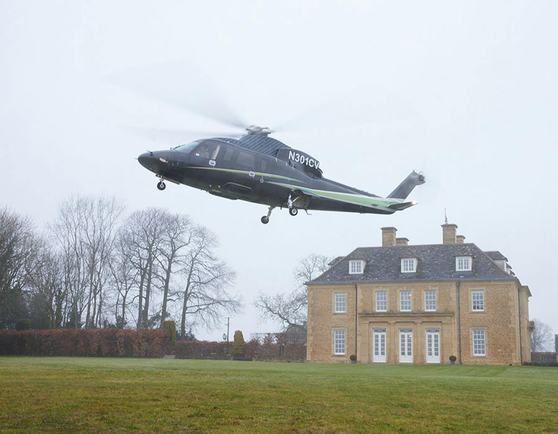 s76 landing on the lawn of a large house