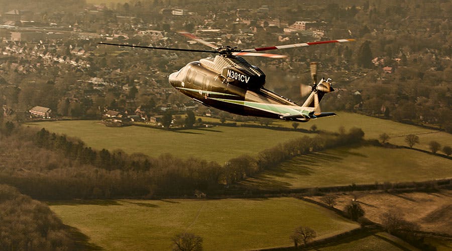 s76 flying over green country side towards a town