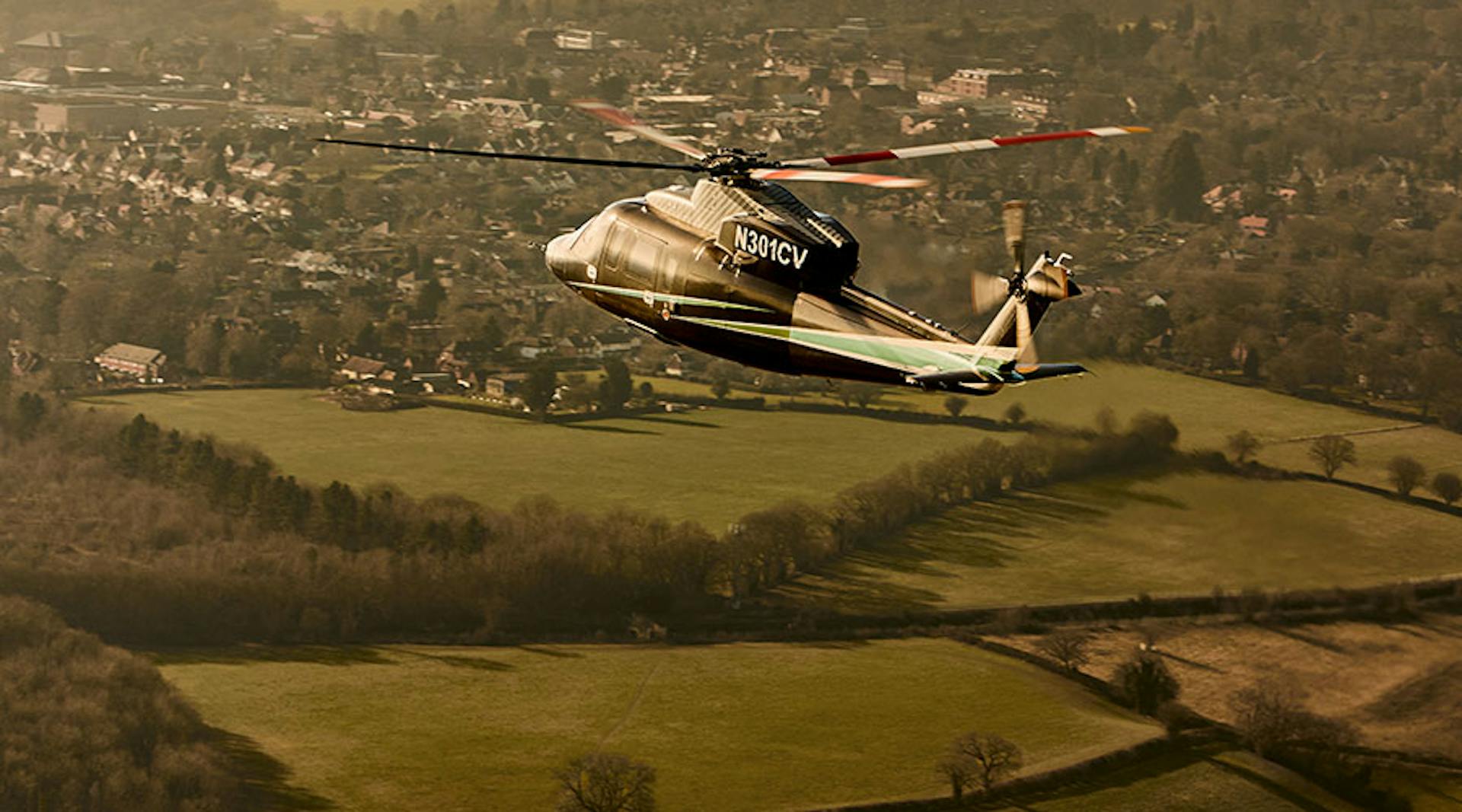 s76 flying over green country side towards a town
