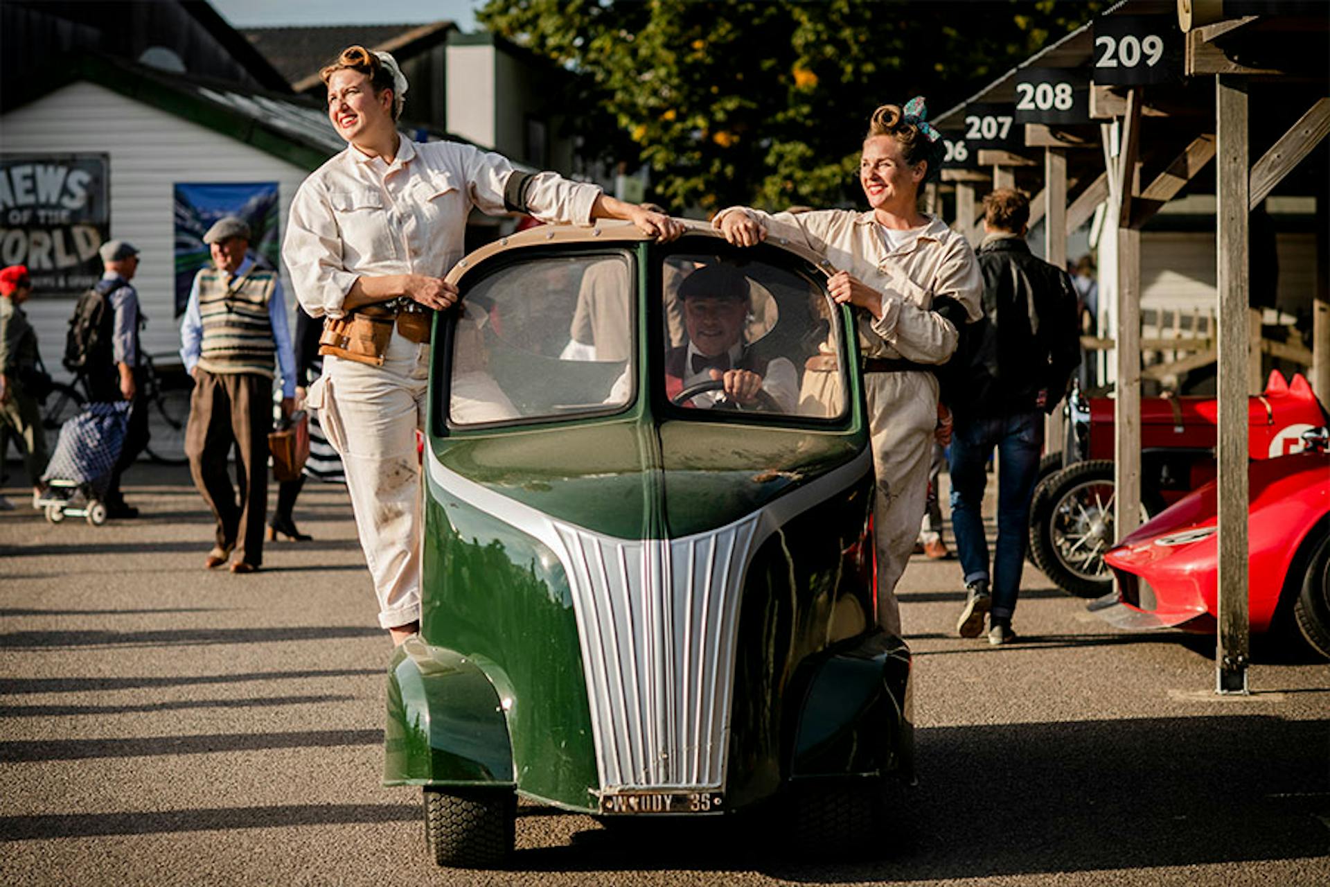 people posing on the sides of a unique looking small car