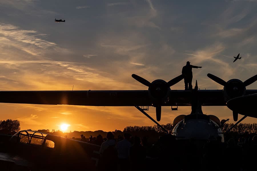 silhouette of prop plane and someone standing on it with others flying in the sky