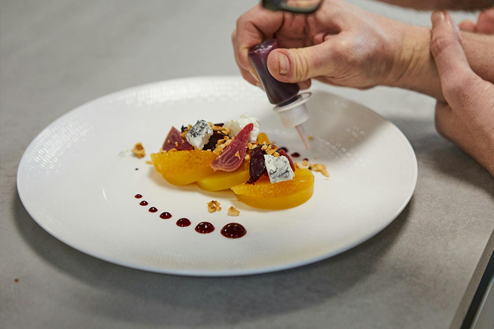 fancy food being plated, garnished with drops of dark red liquid