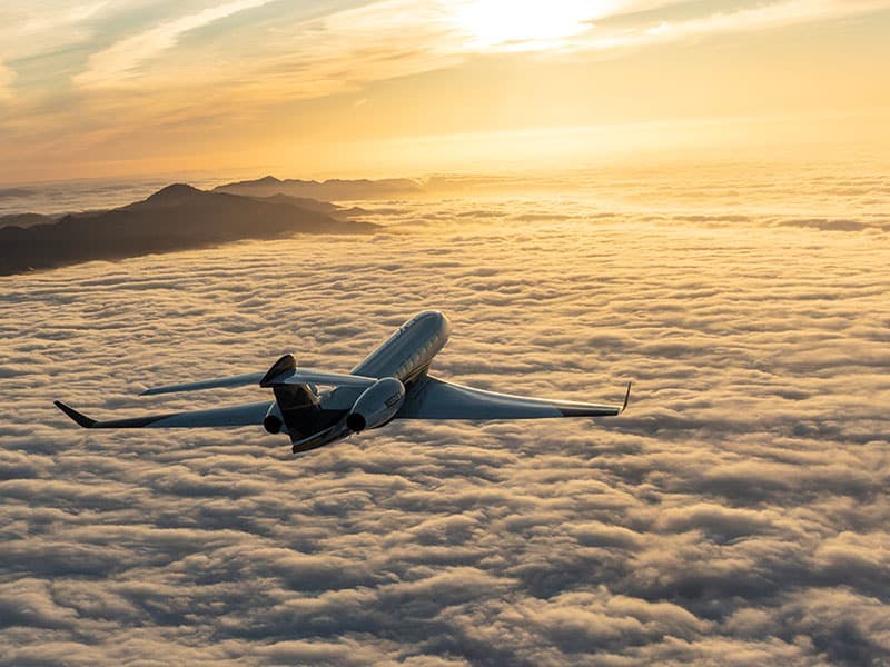 Flexjet aircraft flying over the clouds towards the sunset