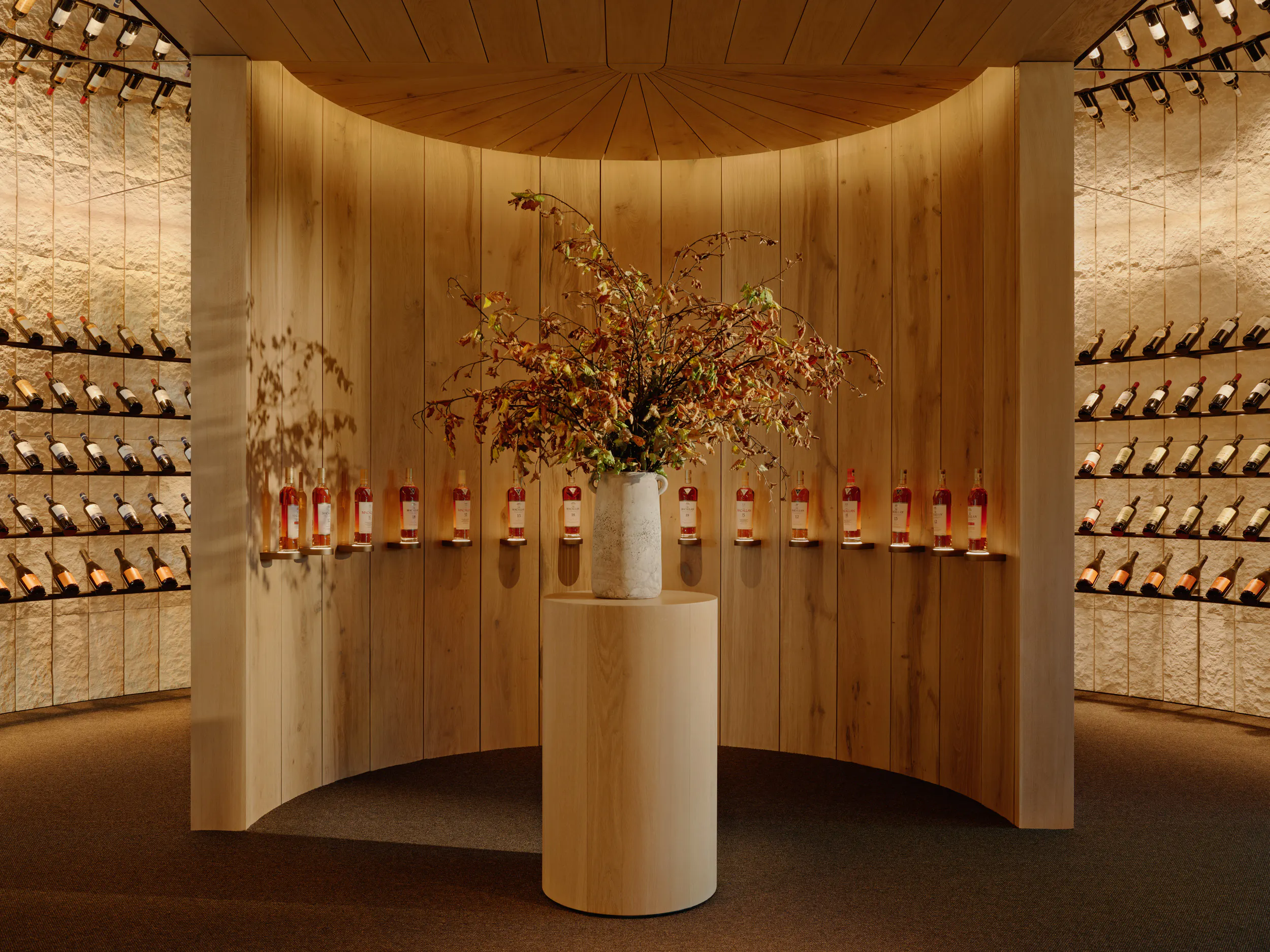 A circular room with wine on around the walls and an inner partition with wine and a vase of flowers