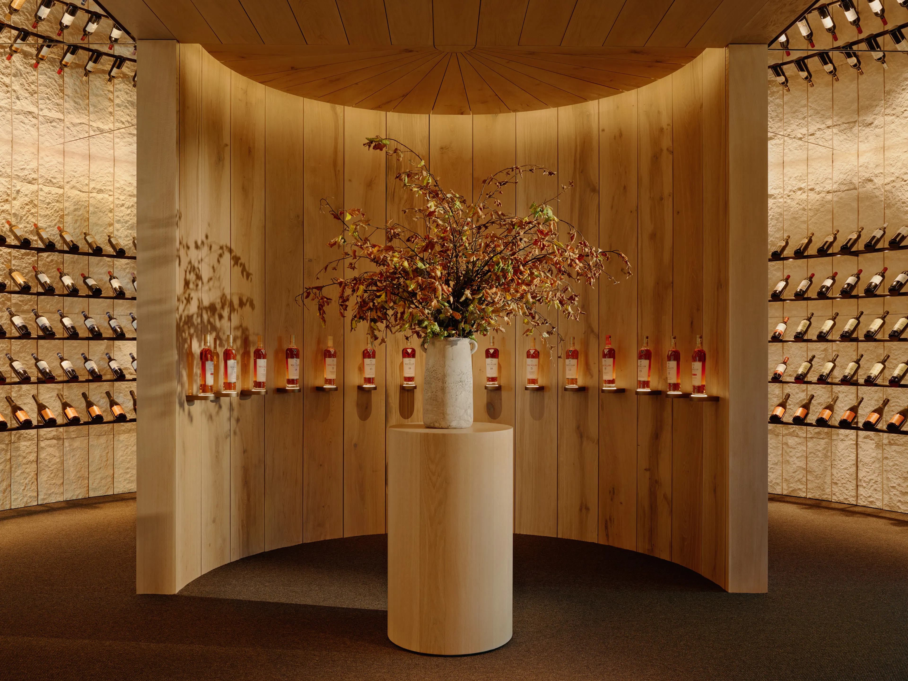 A circular room with wine on around the walls and an inner partition with wine and a vase of flowers