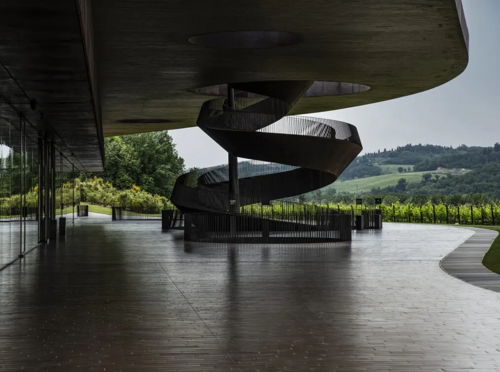 A spiral staircase ascends to a higher level from an outdoor patio overlooking green hills