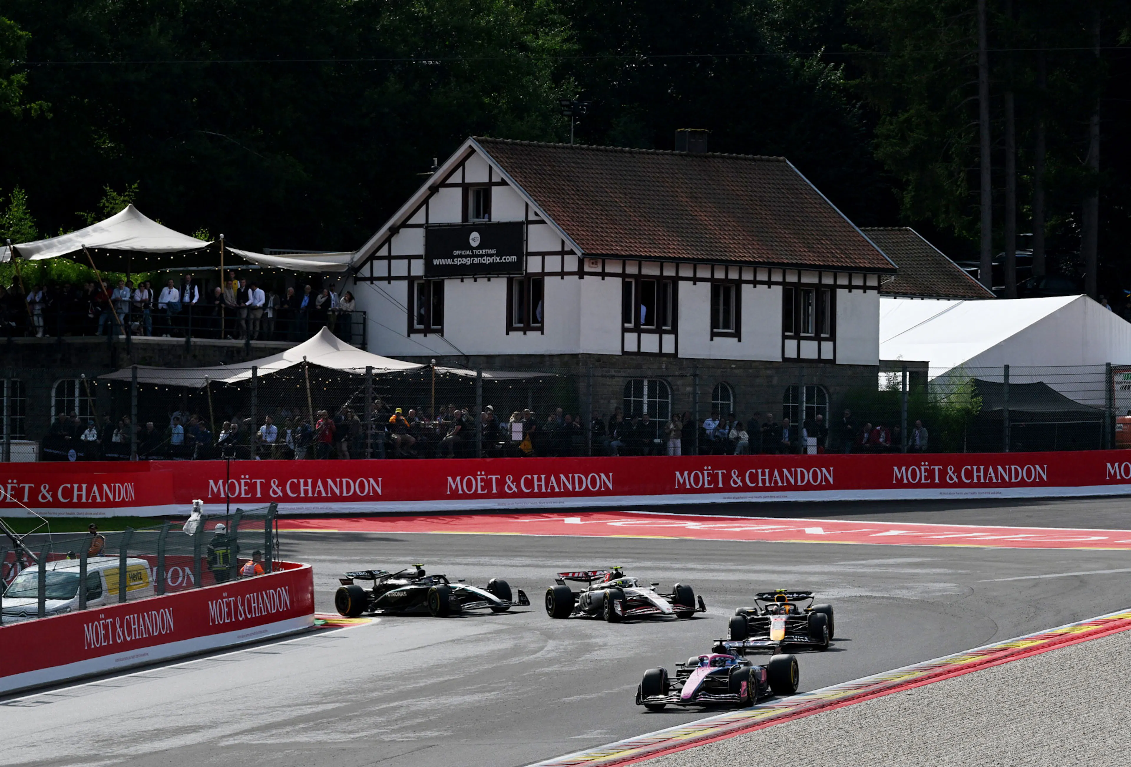 F1 cars rounding a corner with a Belgian building in the background