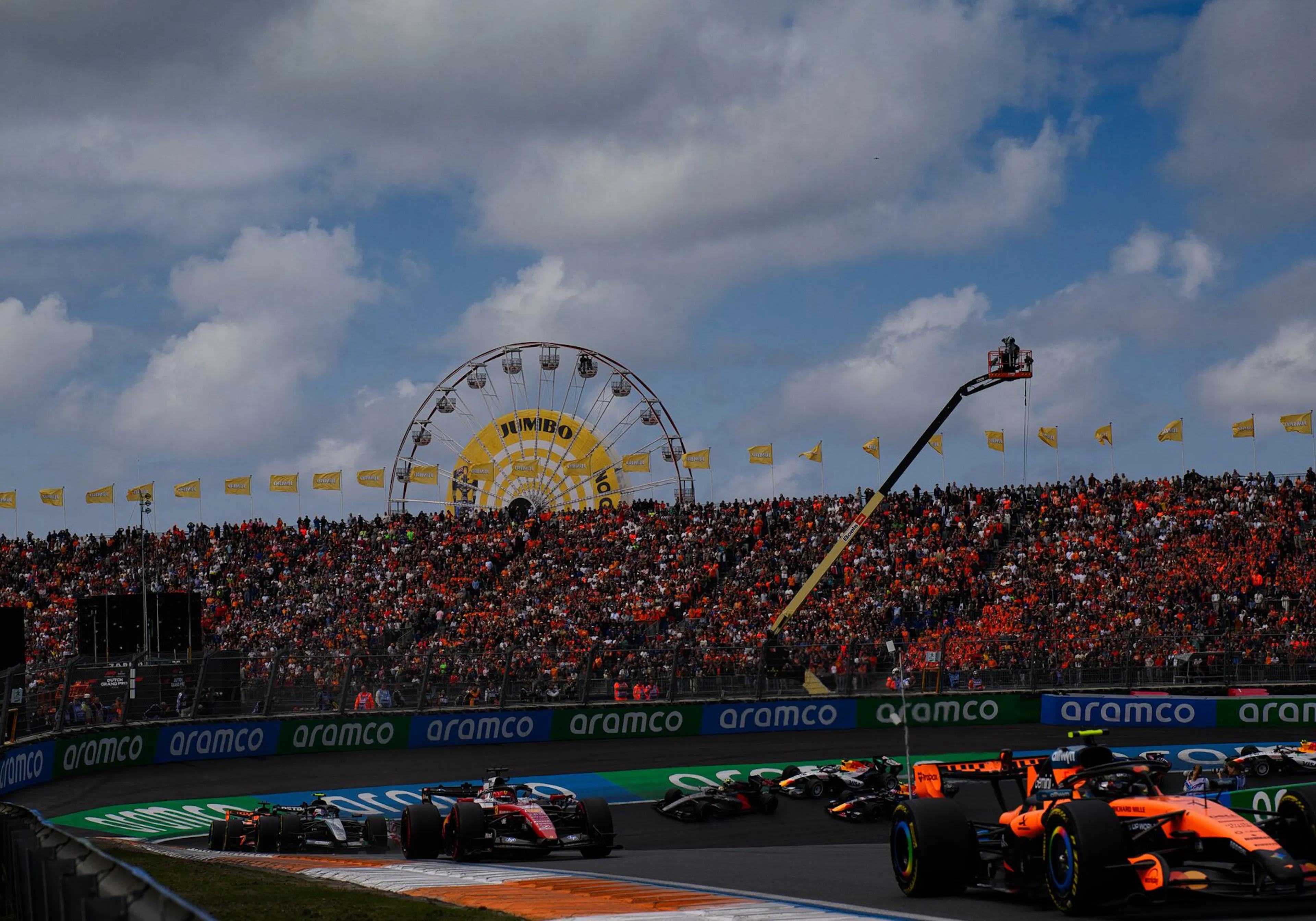 Crowd in the stands watching F1 cars zip around a corner