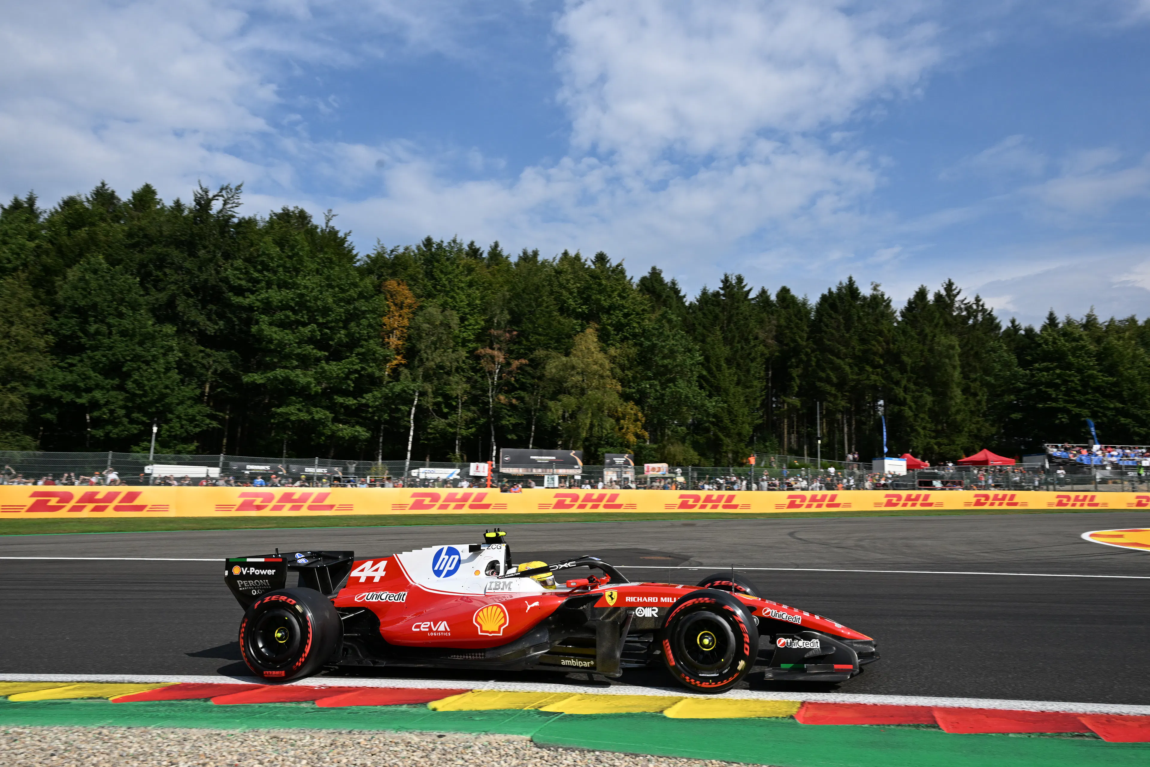 Red and white F1 race car driving on the track with a forest in the background