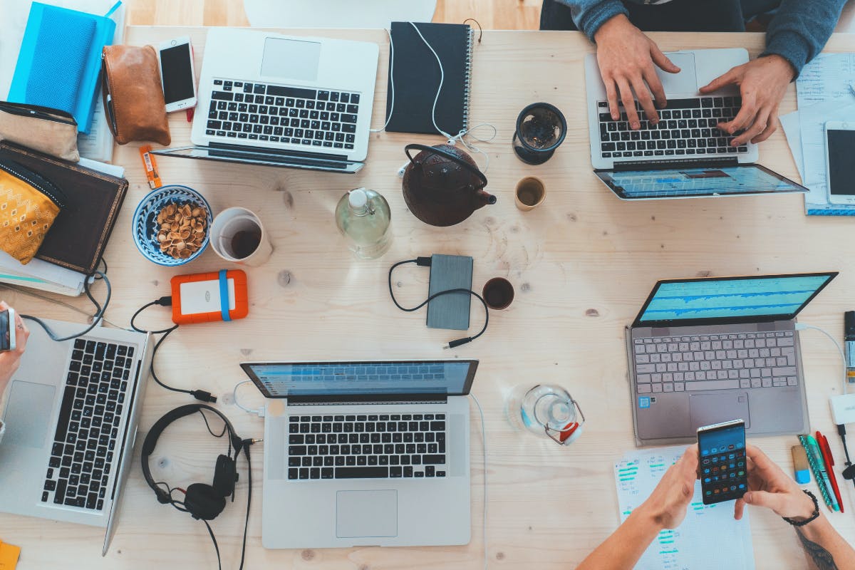 Mehrere Menschen sitzen an einem Tisch und nutzen Laptops und Smartphones Mehrere Menschen sitzen an einem Tisch und nutzen Laptops und Smartphones