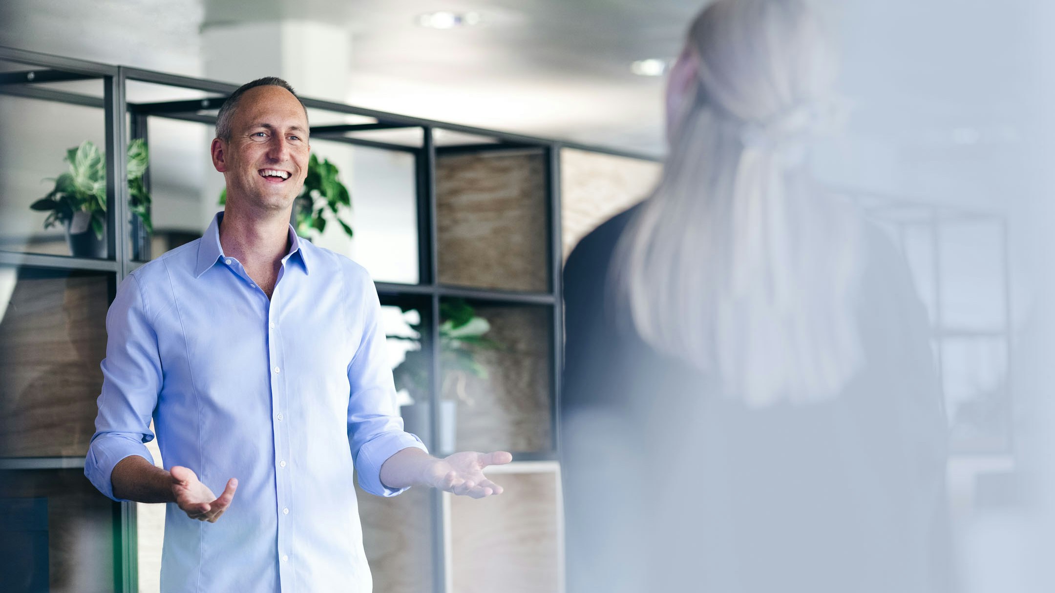 Man with shirt in front of shelf talking to woman