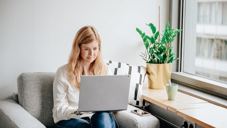 Blonde Frau arbeitet in grauem Sessel am Laptop