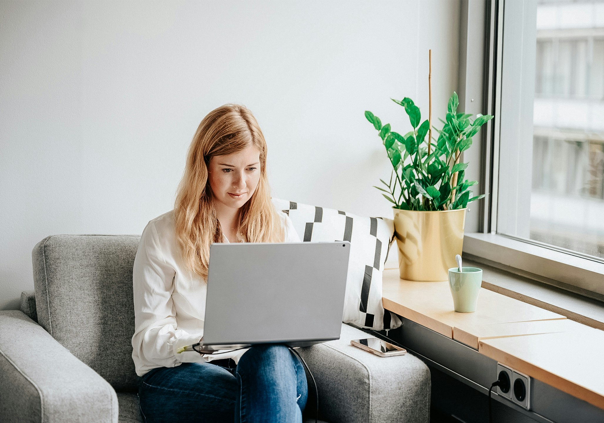 Blonde Frau arbeitet in grauem Sessel am Laptop