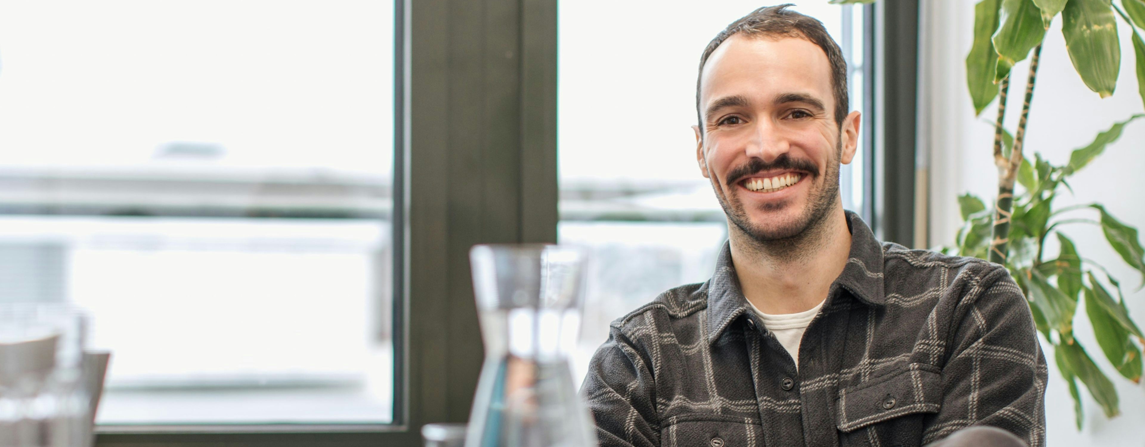 Falk Schuhmacher from GLS wears a lumberjack shirt and smiles at the camera