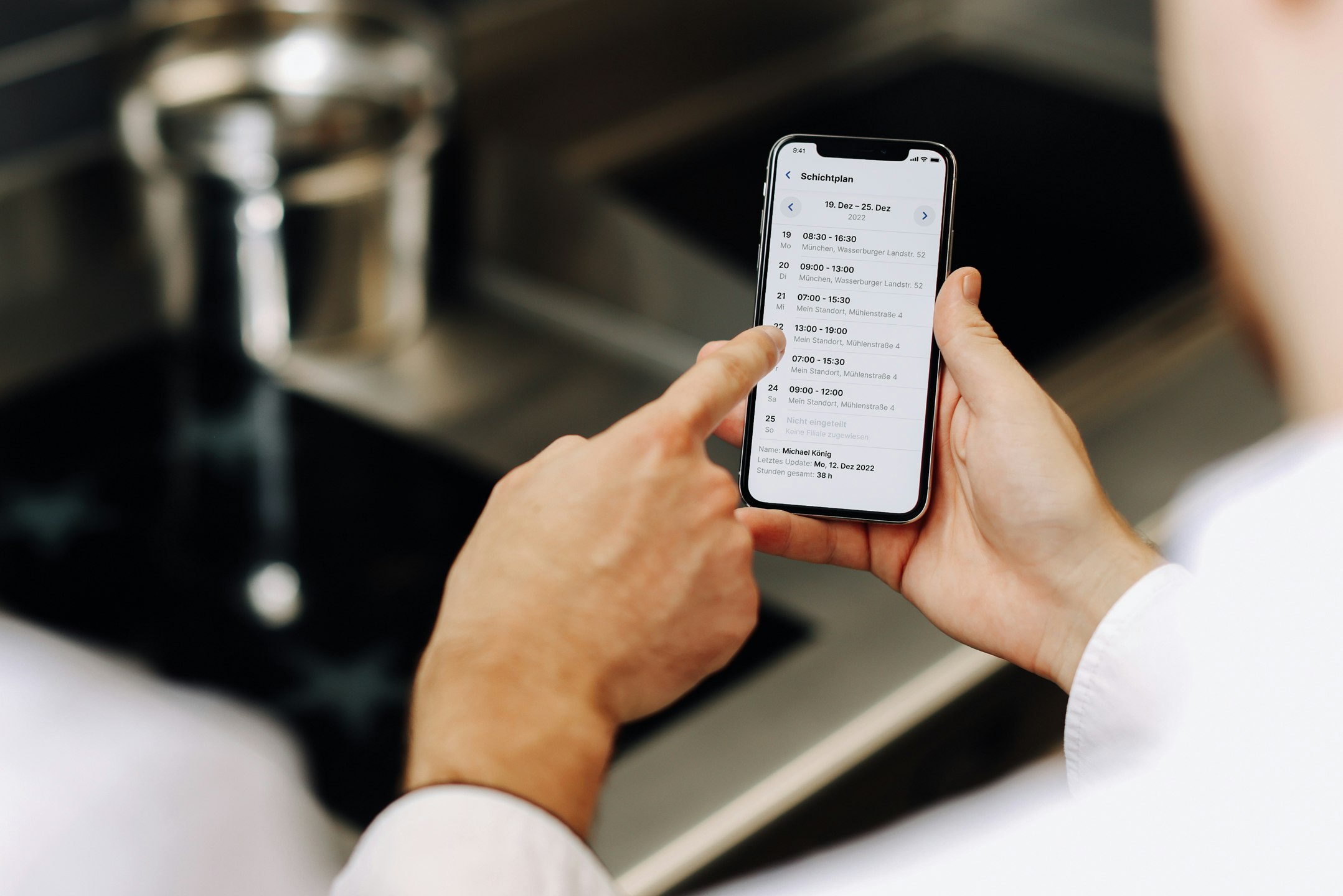 Smartphone-Display zeigt Schichtplan und IndustriekĂĽche im Hintergrund
