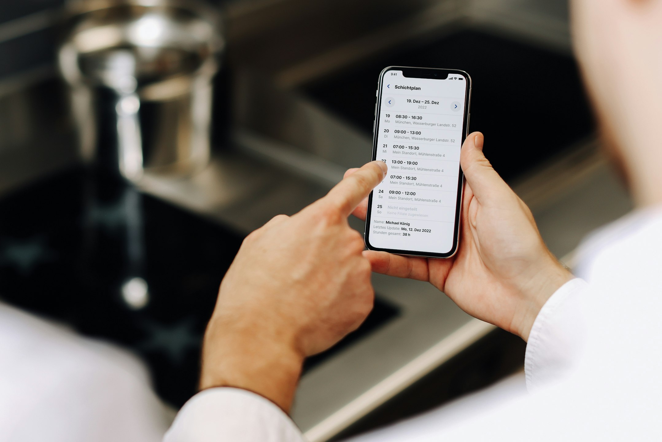 Smartphone-Display zeigt Schichtplan und Industrieküche im Hintergrund