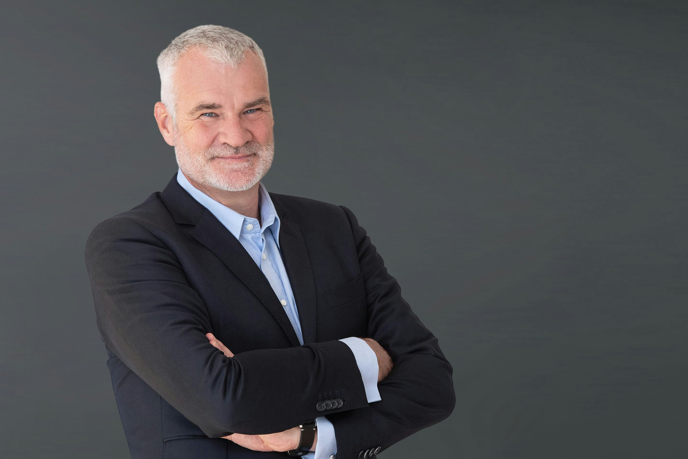 Jörg Walz smiling in camera wearing a black blazer and crossing arms