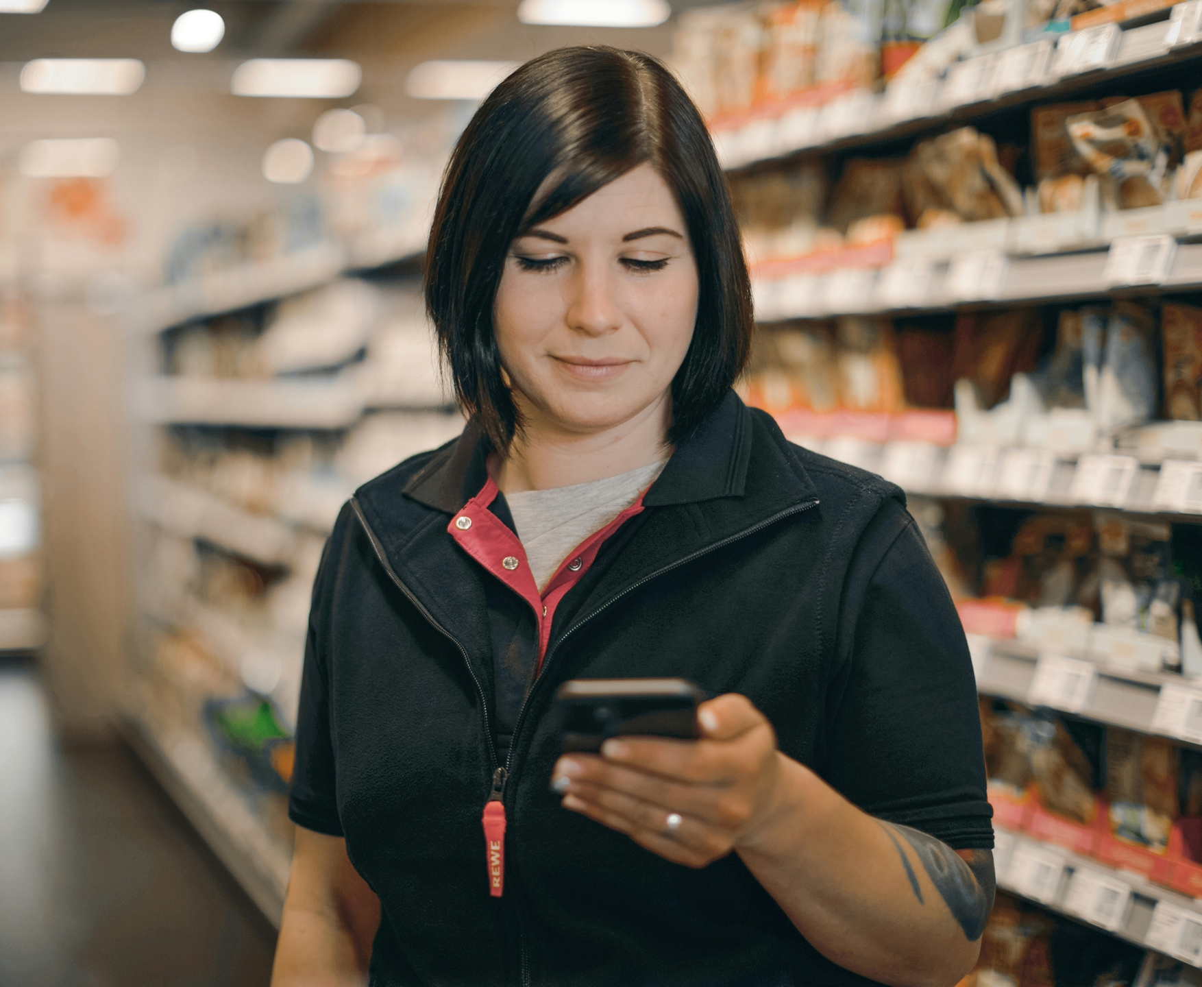 REWE employe standing in the store looking at her phone