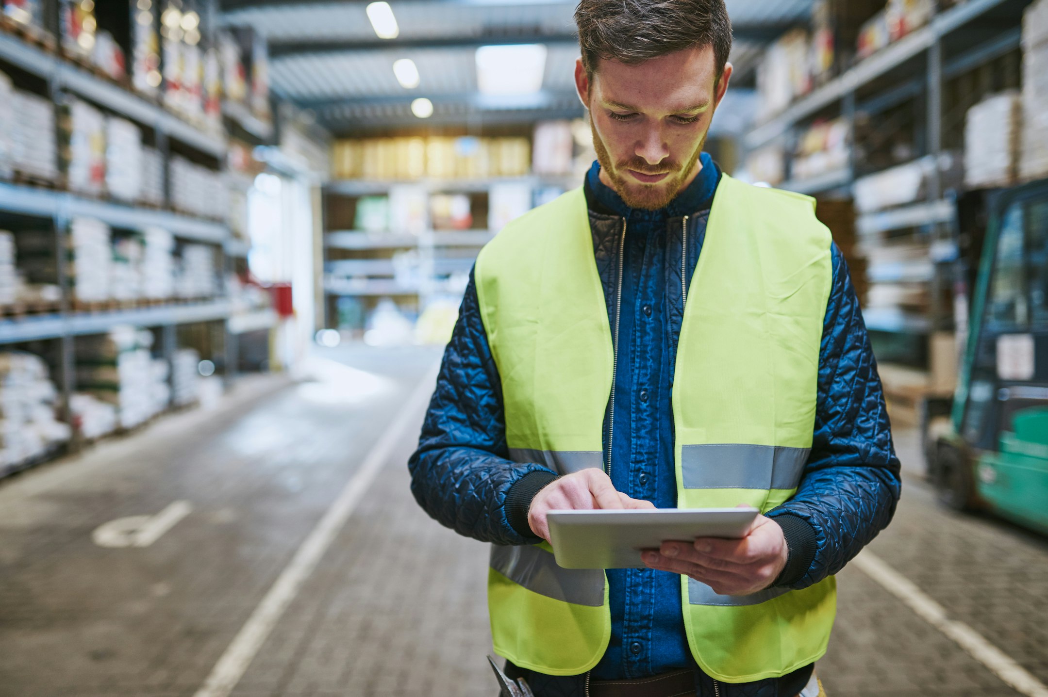 Worker in a hi-vis vest on the warehouse floor using a tablet