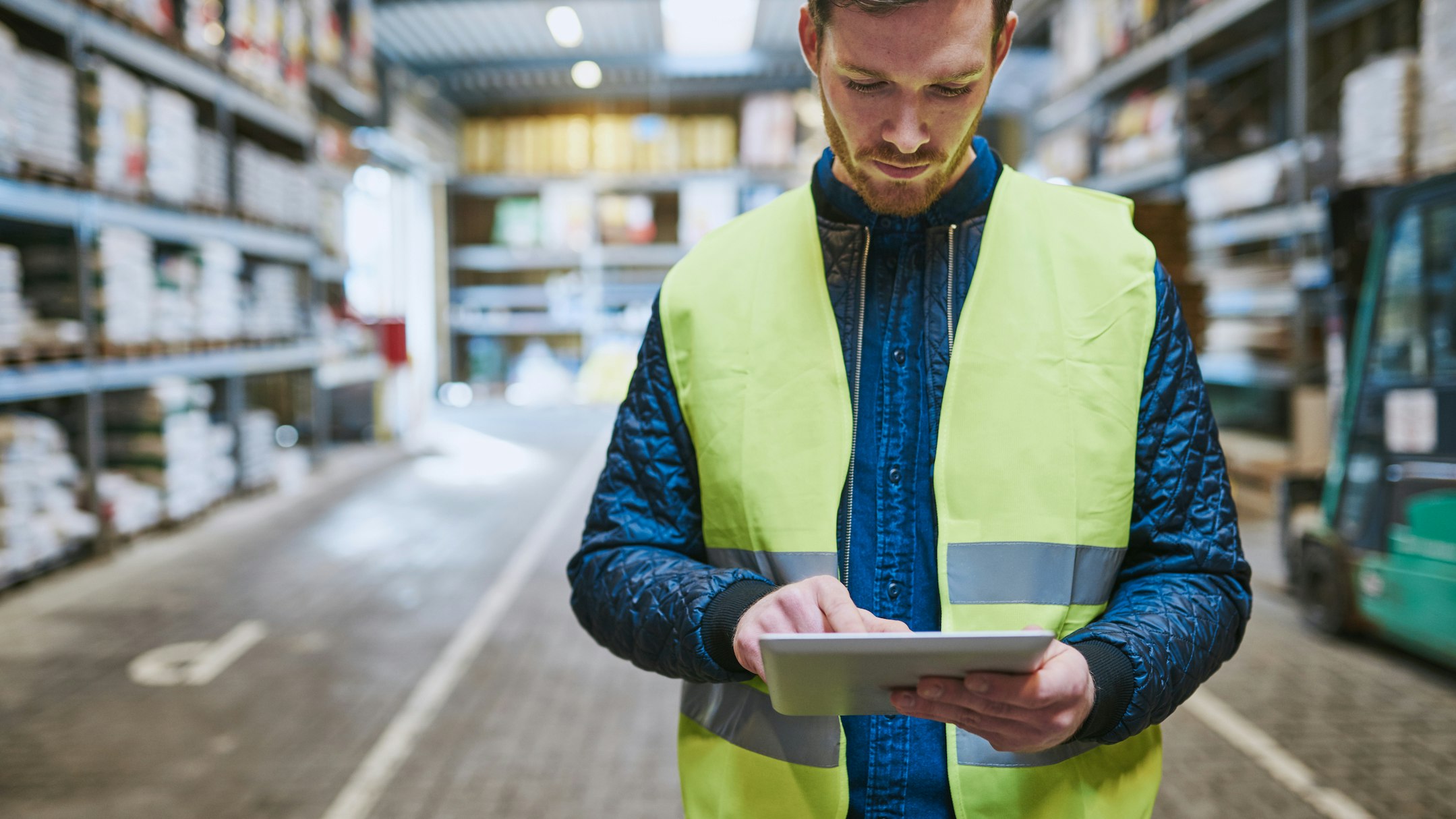 Worker in a hi-vis vest on the warehouse floor using a tablet