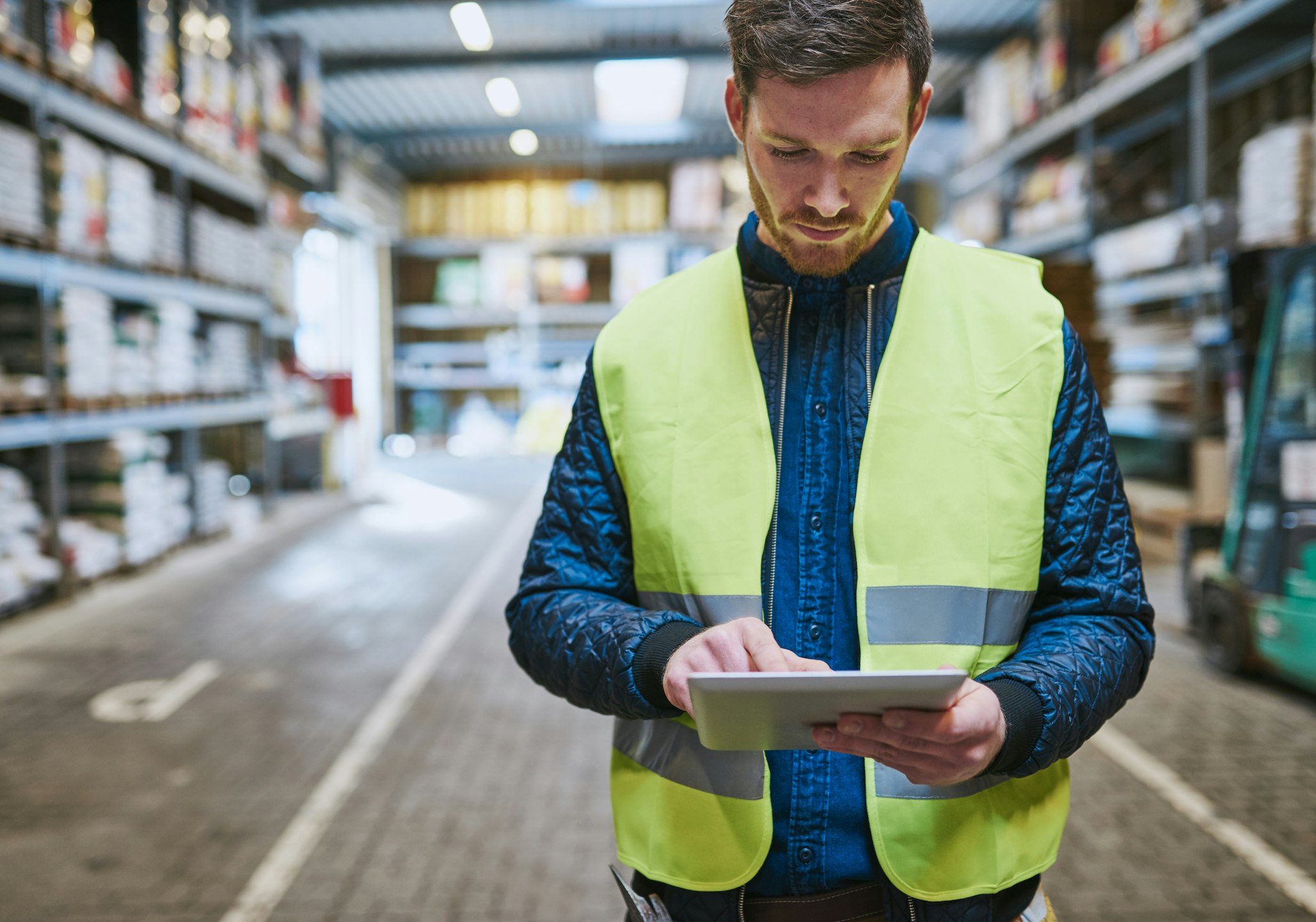 Worker in a hi-vis vest on the warehouse floor using a tablet