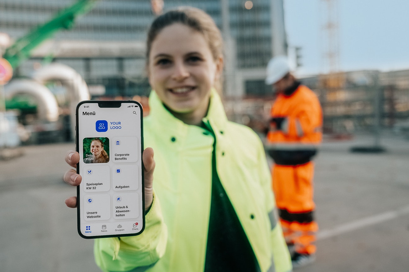 Arbeiterin auf Baustelle zeigt Mitarbeiter-App in die Kamera 