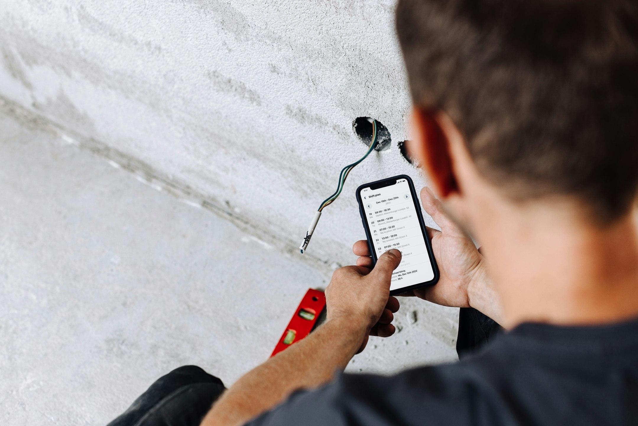 A construction worker photographed from behind looking at his work schedule on his phone