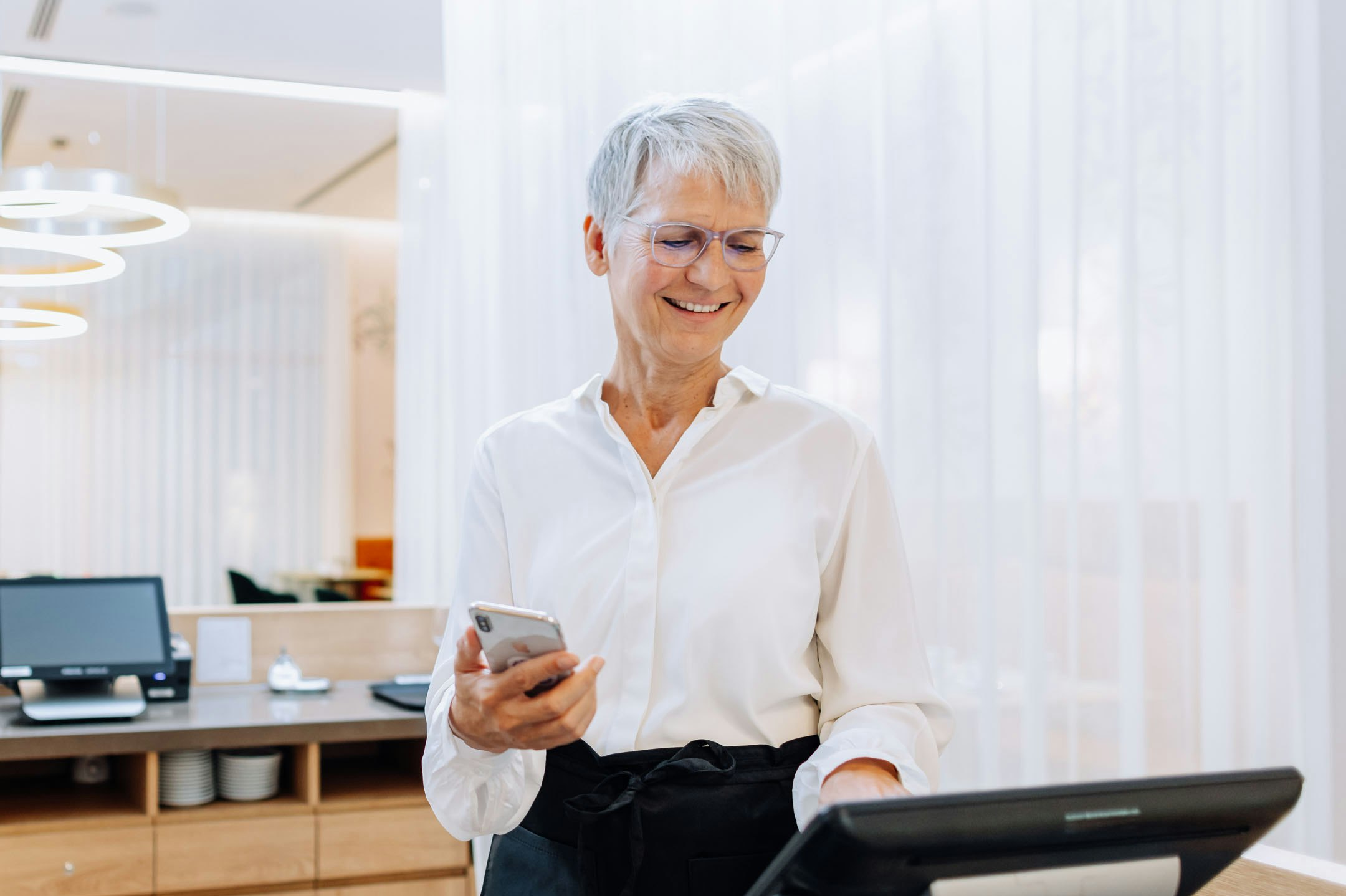 Hotel management assistant stands at the reception with smartphone and booking device