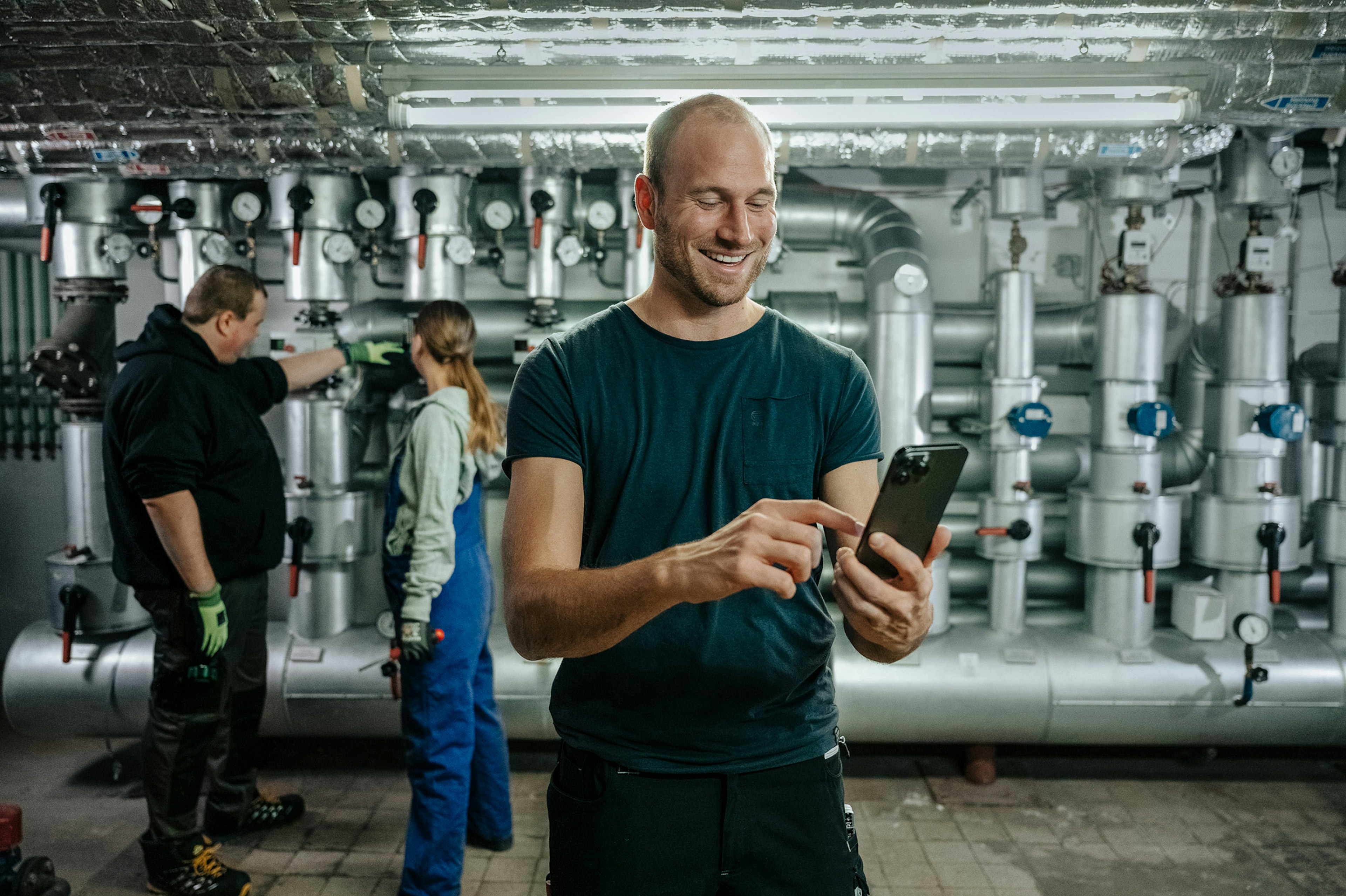 Arbeiter vor eine Industrieanlage tippt lächelnd in sein Smartphone