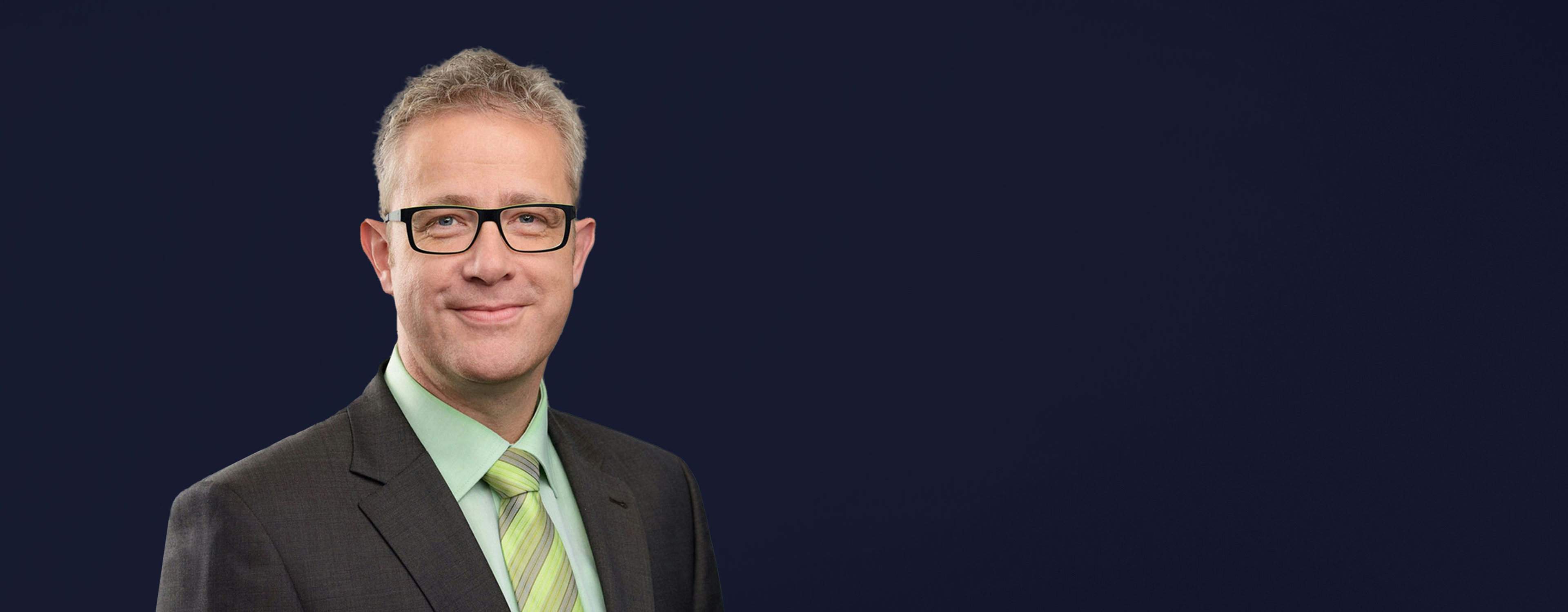 Michael Heß mh plus smiling into camera with black glasses and green tie