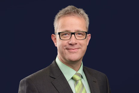 Michael Heß mh plus smiling into camera with black glasses and green tie
