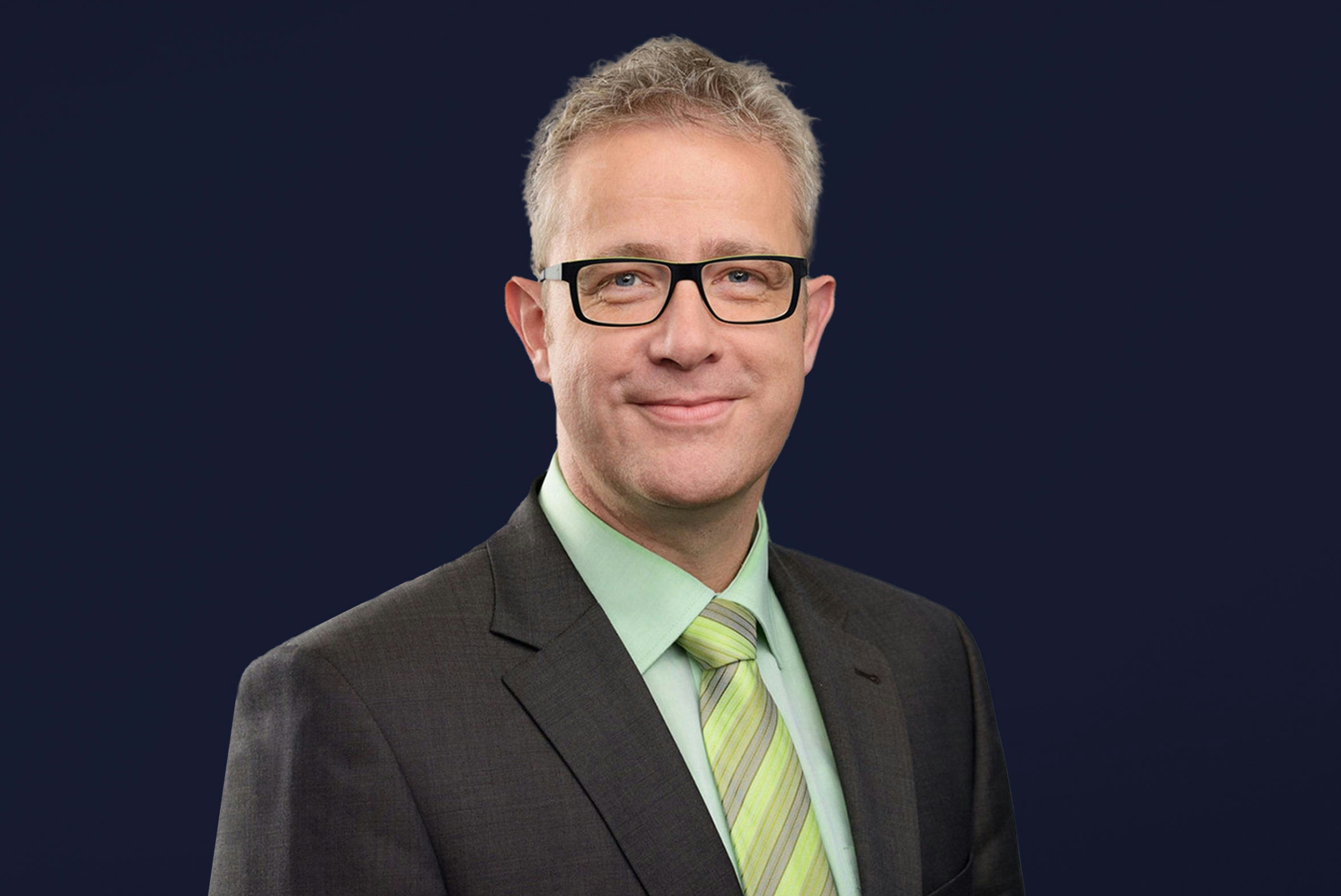 Michael Heß mh plus smiling into camera with black glasses and green tie