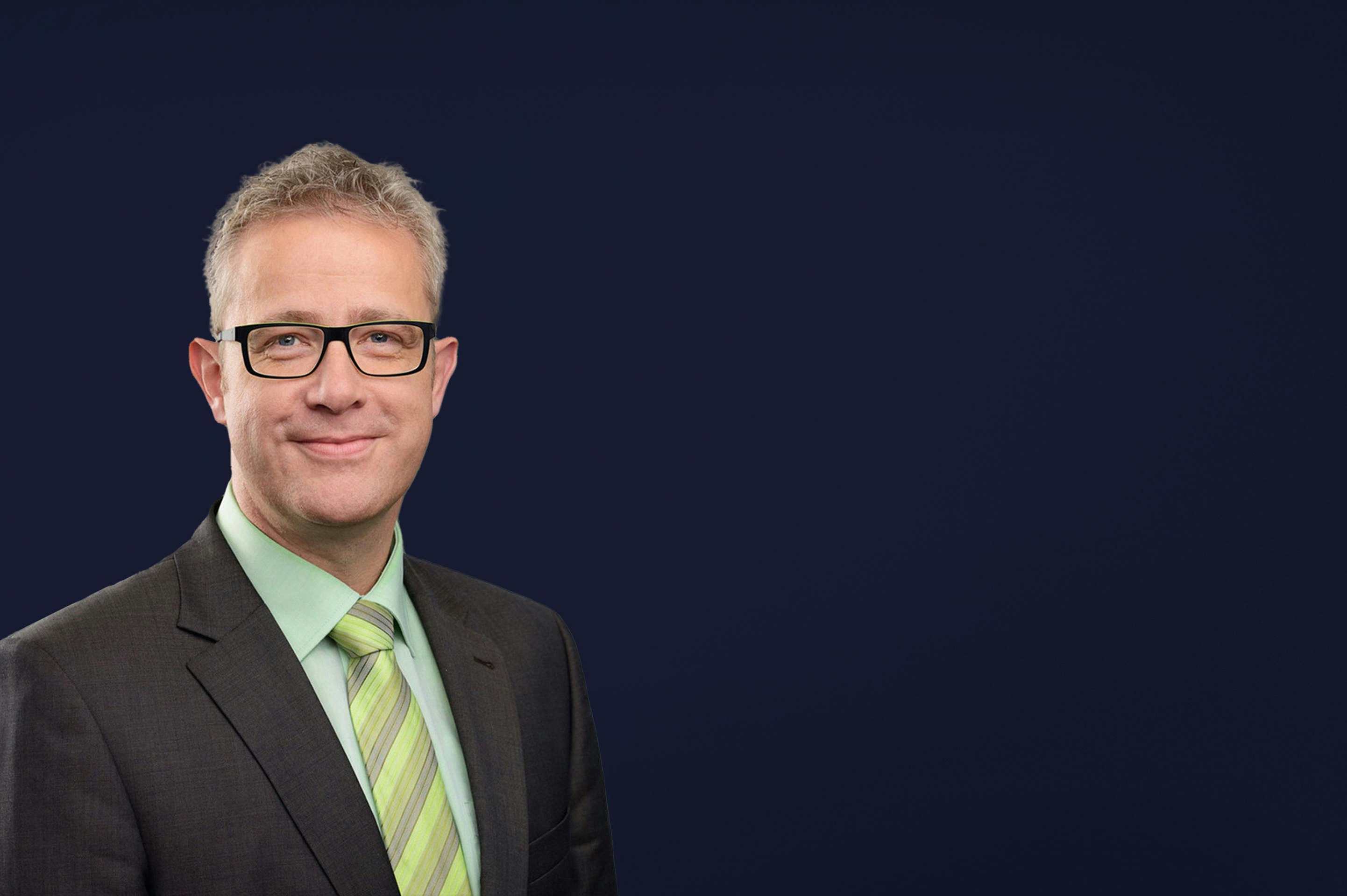 Michael Heß mh plus smiling into camera with black glasses and green tie