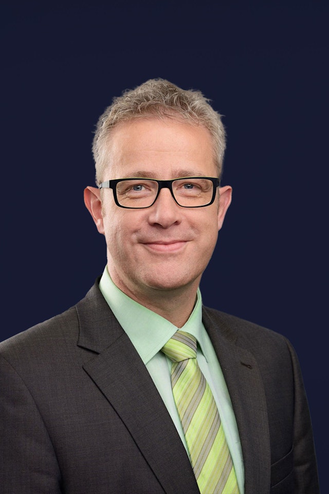 Michael Heß mh plus smiling into camera with black glasses and green tie